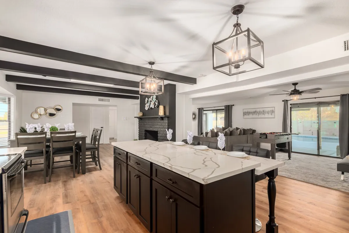 This image showcases an open-concept layout that seamlessly connects the kitchen, dining area, living room seating, and a fireplace. Large windows invite natural light, enhancing the welcoming atmosphere. The spacious kitchen island and adjacent dining space are perfect for cooking, dining, and socializing all in one unified area.