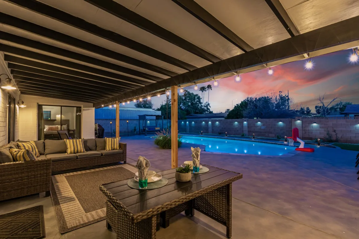 An inviting backyard scene featuring a sparkling swimming pool surrounded by comfortable wicker seating, an outdoor dining table, and soft evening lighting. The space is set up for relaxation and social gatherings, with the pool as the centerpiece for fun family activities.