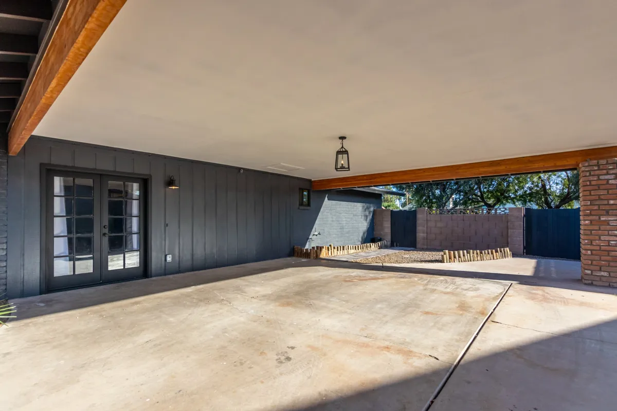 A covered patio with exposed beams, a brick wall, French doors, and a hanging light fixture creates an inviting transition from indoor to outdoor living. The space is ideal for family barbecues or relaxed outdoor activities at any time of day.