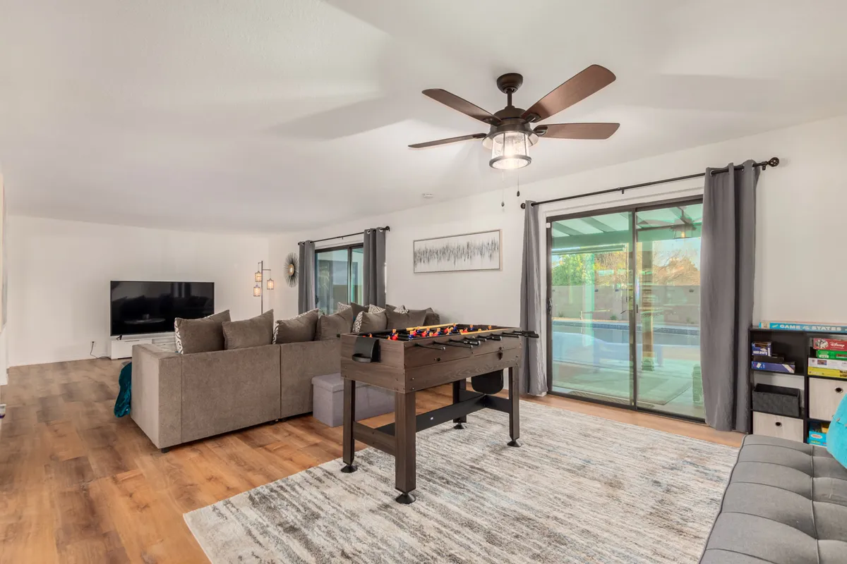 A bright and lively interior game room featuring a cozy seating area, a foosball table, large sliding glass doors opening to the outside, and a TV. The space radiates playfulness and invites guests to engage in games and entertainment, echoing the idea of indoor fun for all ages.