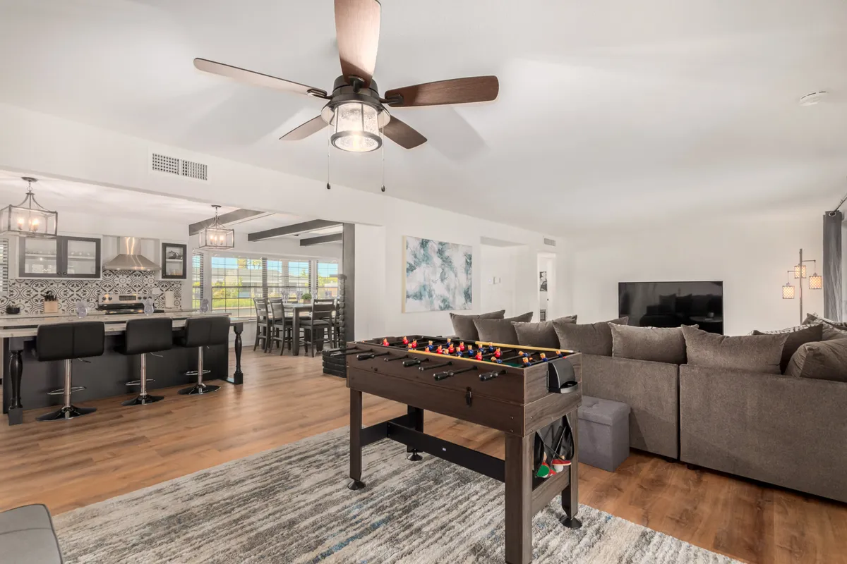 A vibrant, playful space featuring a foosball table, comfortable couch, and a view into a modern kitchen area. The area is designed for fun game nights, socializing, and casual relaxation, encouraging both active and laid-back family moments.