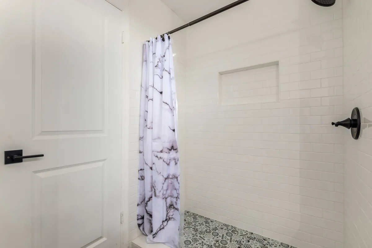 A clean, modern bathroom with a decorative tile floor, elegant shower curtain, and a sleek showerhead. The space feels fresh and spa-like, ideal for moments of relaxation.