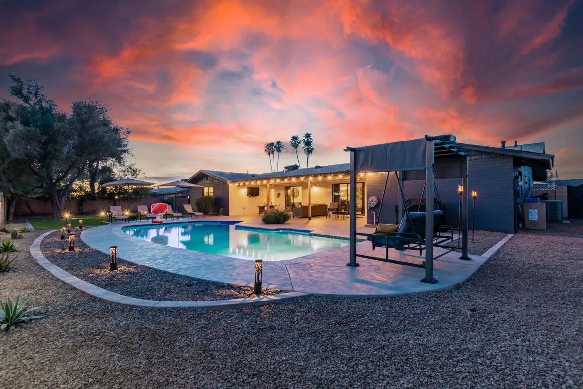 The photo captures a tranquil backyard scene at sunset, with a sparkling swimming pool, palm trees, stylish seating, and a glowing sky. The setup is perfect for entertaining guests, relaxing after a day at the ballpark, or enjoying sunset swims and evening gatherings.