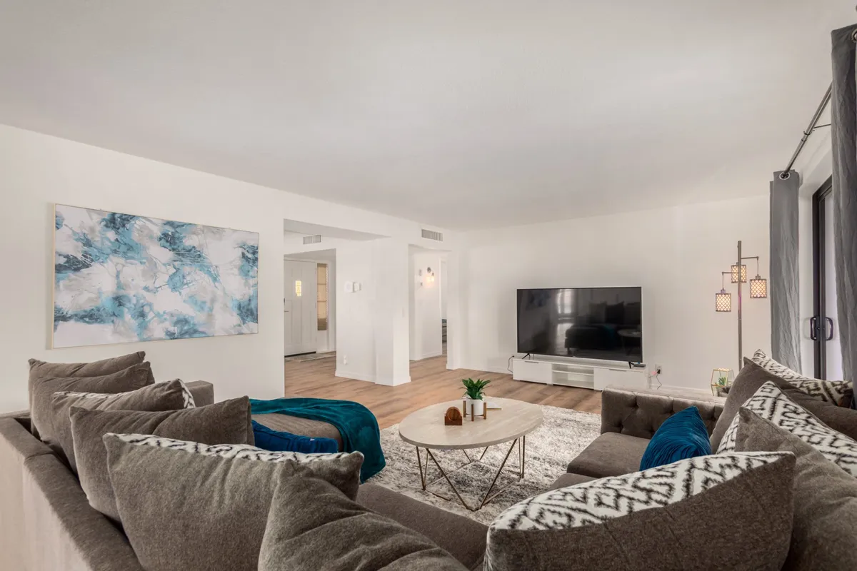 A cozy, contemporary living area with a stylish sofa adorned with decorative pillows, a coffee table, wall art, and a television. The room exudes comfort and is ideal for relaxing or entertaining guests.