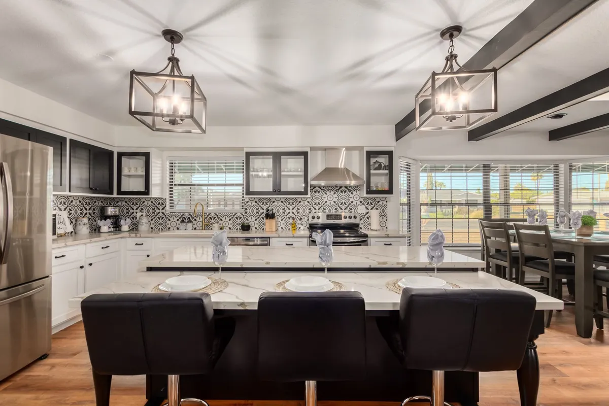 A sophisticated kitchen scene featuring a large kitchen island, stylish pendant lights, and a distinctive black and white patterned backsplash. The space is set up for cooking family meals, casual dining, and entertaining guests, with plenty of prep space and modern amenities.