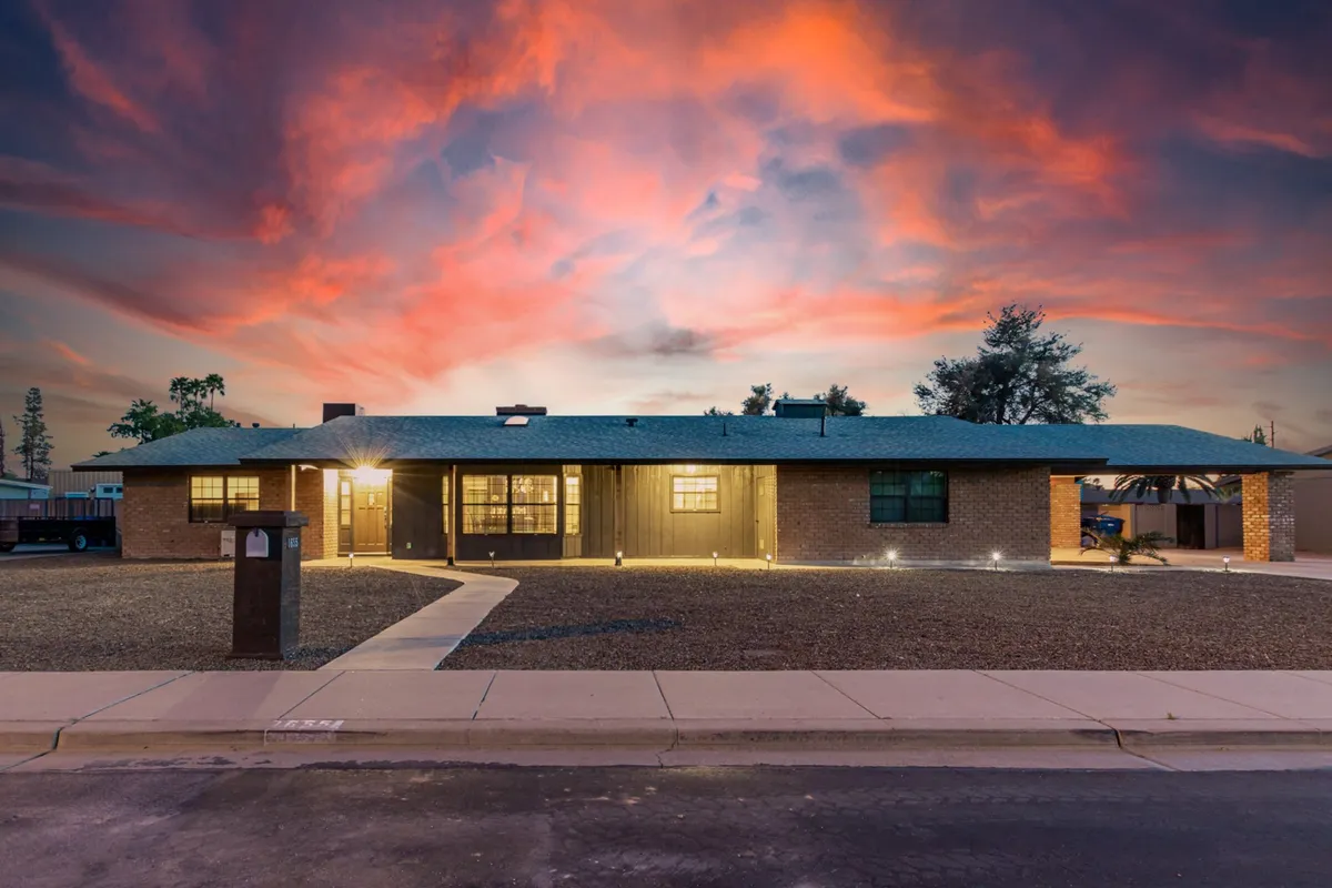 The image shows the house facade at dusk, set against a colorful sky with attractive landscaping in the foreground. The warm exterior lighting creates a welcoming ambiance, hinting at an inviting space to relax after a day of adventure.