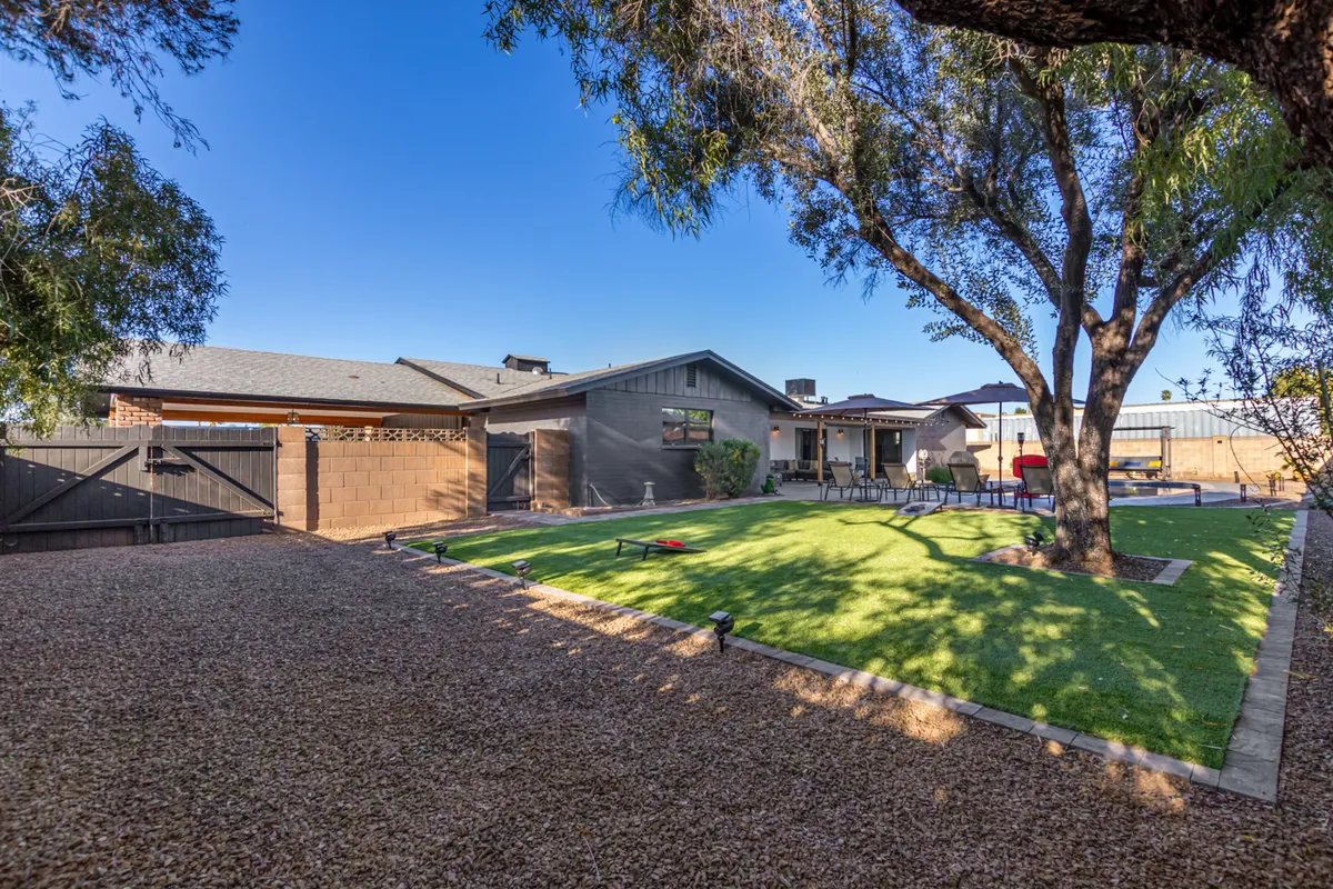 A welcoming exterior scene featuring an expansive lawn area, a large tree providing ample shade, patio seating for outdoor gatherings, and the home’s backdrop. The spaciousness and greenery make it an ideal setting for outdoor play and pet activities, while the patio invites relaxation and social time for owners.